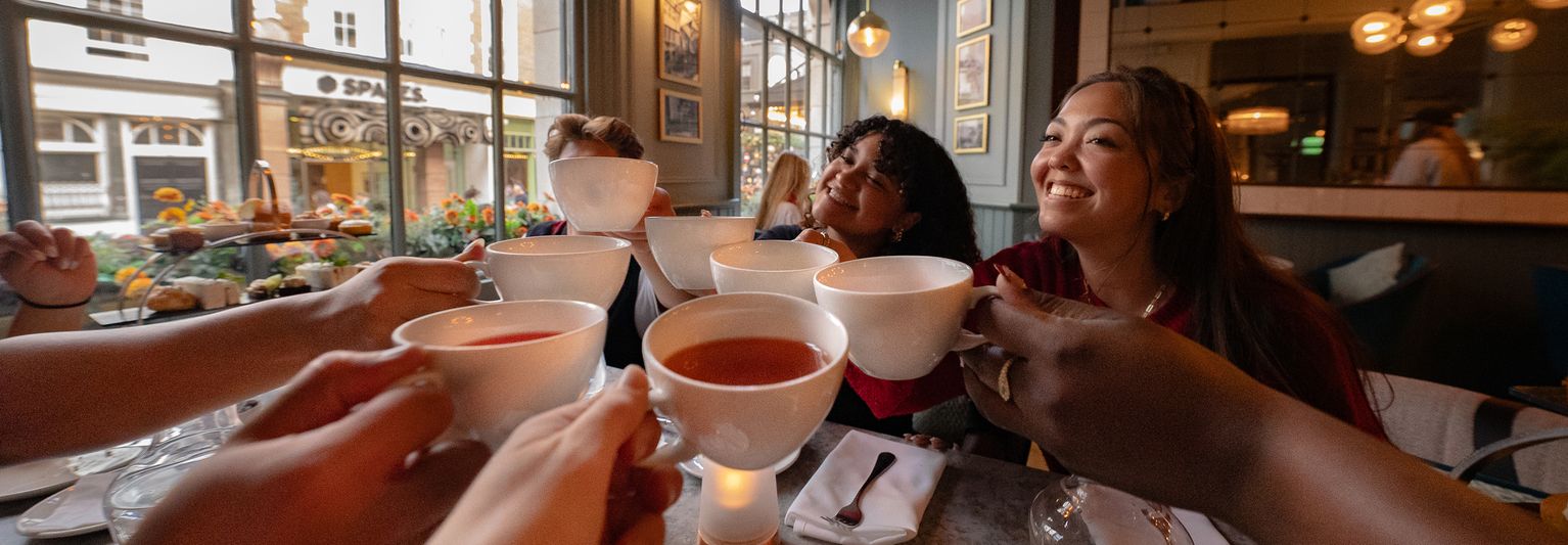 A group of travelers clinking their teacups together in a toast while at afternoon tea in London.