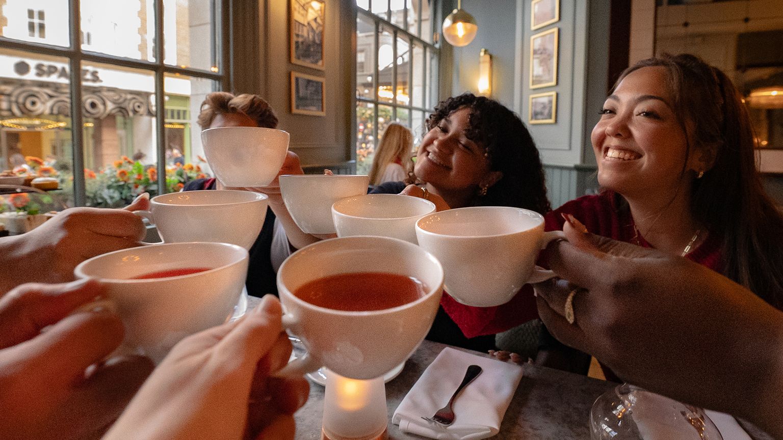 A group of travelers clinking their teacups together in a toast while at afternoon tea in London.