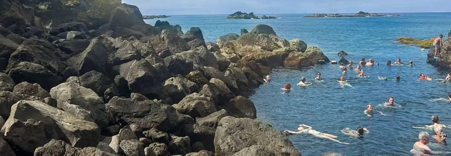 People swimming in a cove next to a rocky island.
