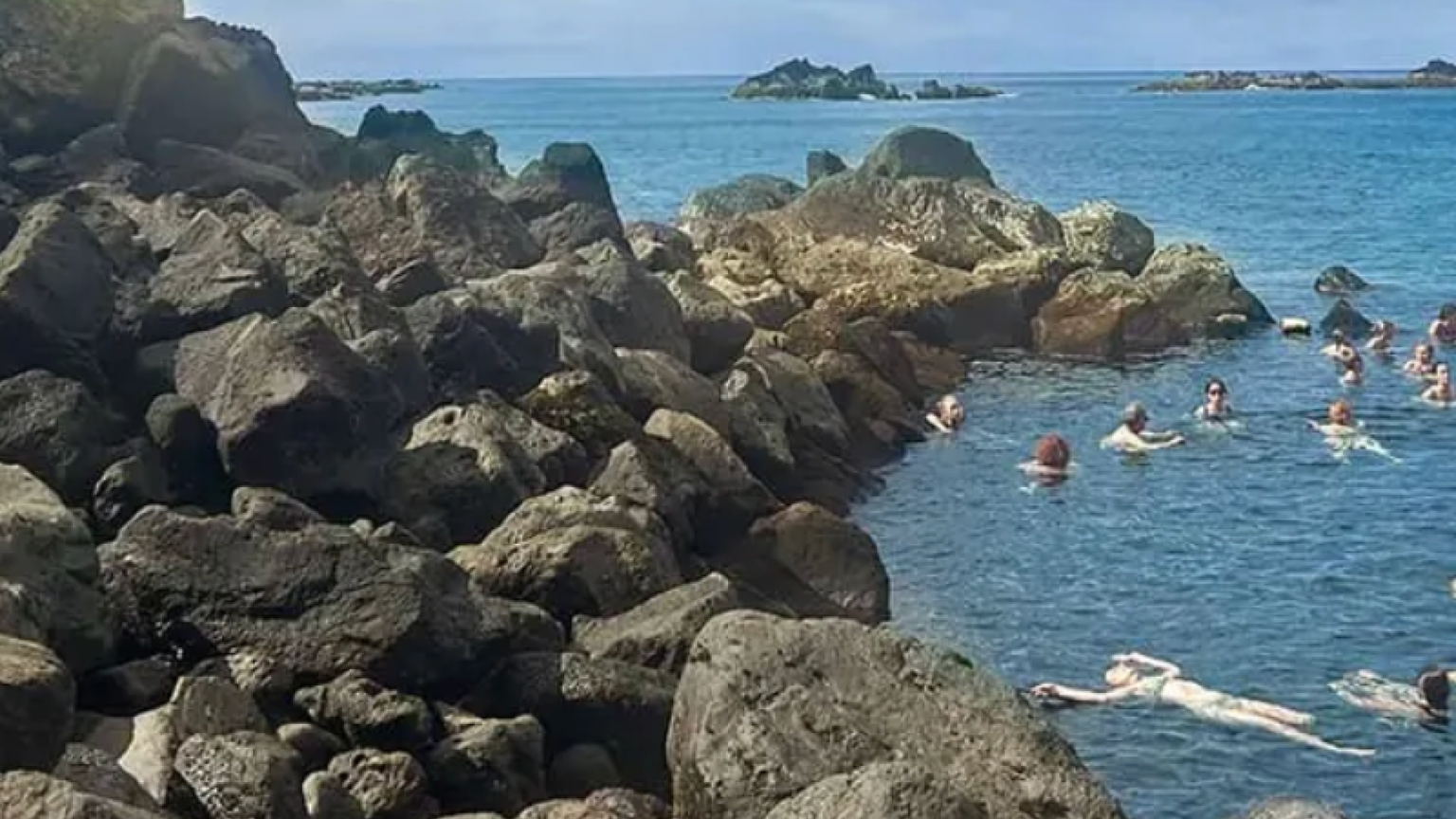 People swimming in a cove next to a rocky island.