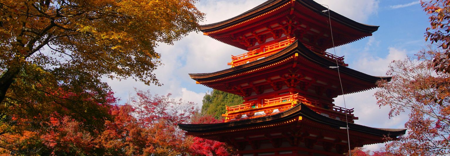 A vibrant red and black pagoda surrounded by colorful autumn trees with a blue sky in the background.