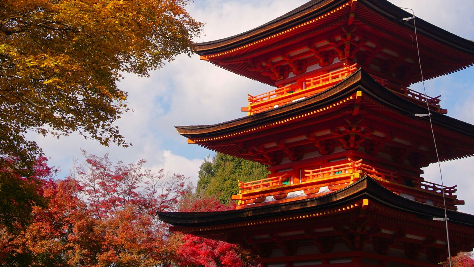 A vibrant red and black pagoda surrounded by colorful autumn trees with a blue sky in the background.