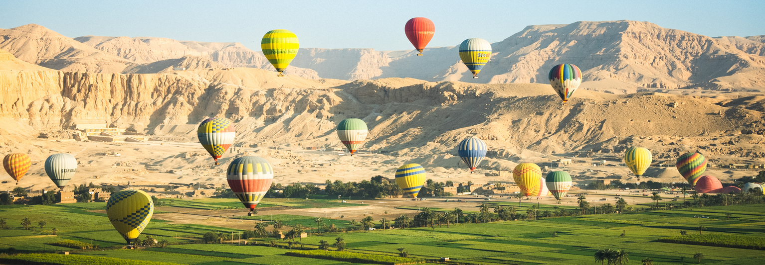 Hot-air balloons flying above a field with the desert in the background.