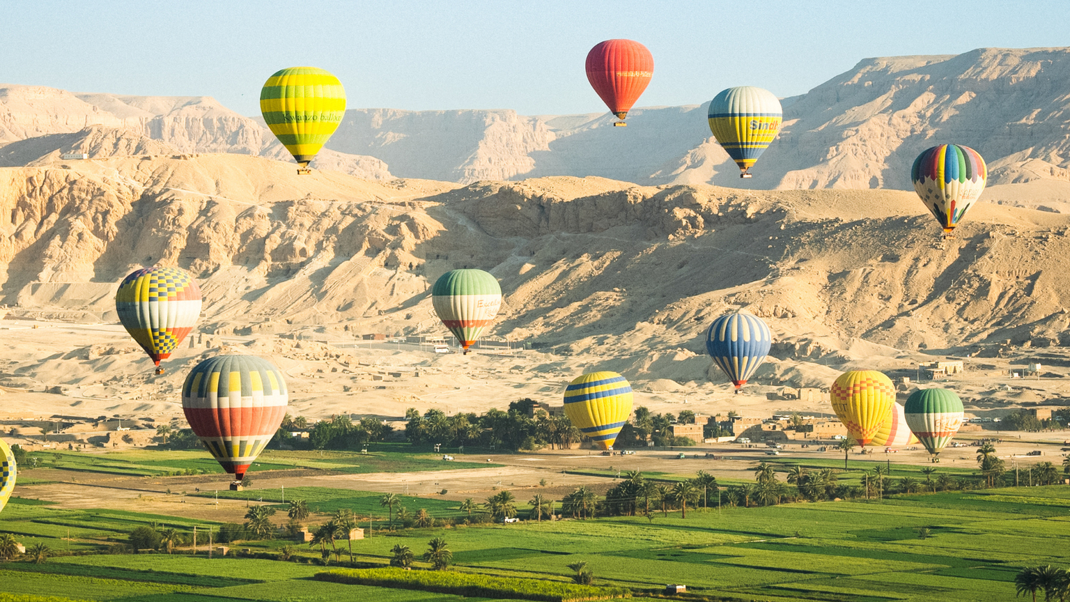 Hot-air balloons flying above a field with the desert in the background.