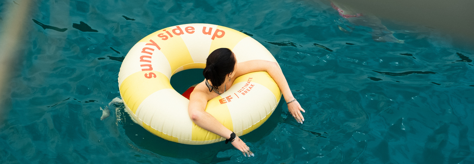 Person in a yellow and white inflatable ring labeled "sunny side up," floating in clear blue water.