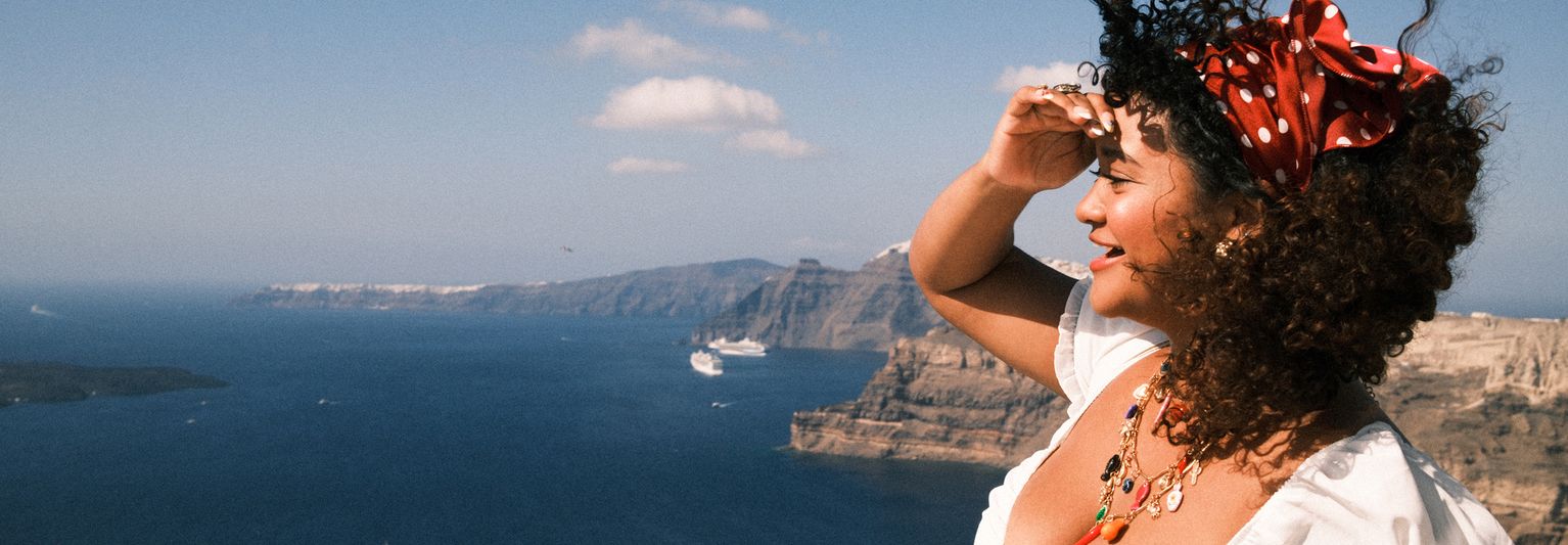 A smiling woman shading her eyes and looking out over Greece's Aegean Sea