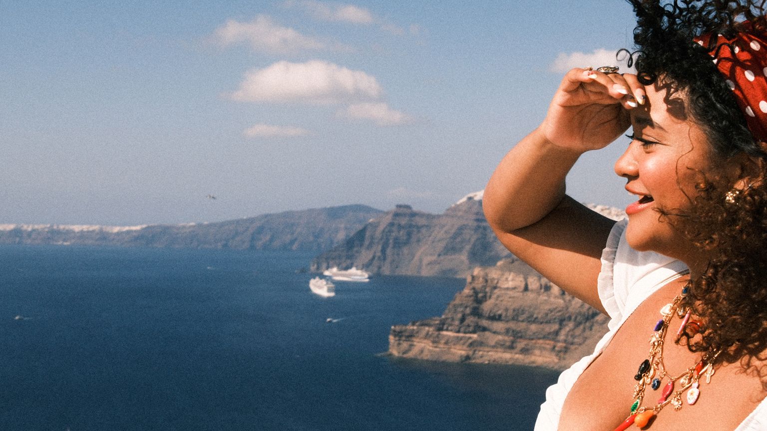 A smiling woman shading her eyes and looking out over Greece's Aegean Sea