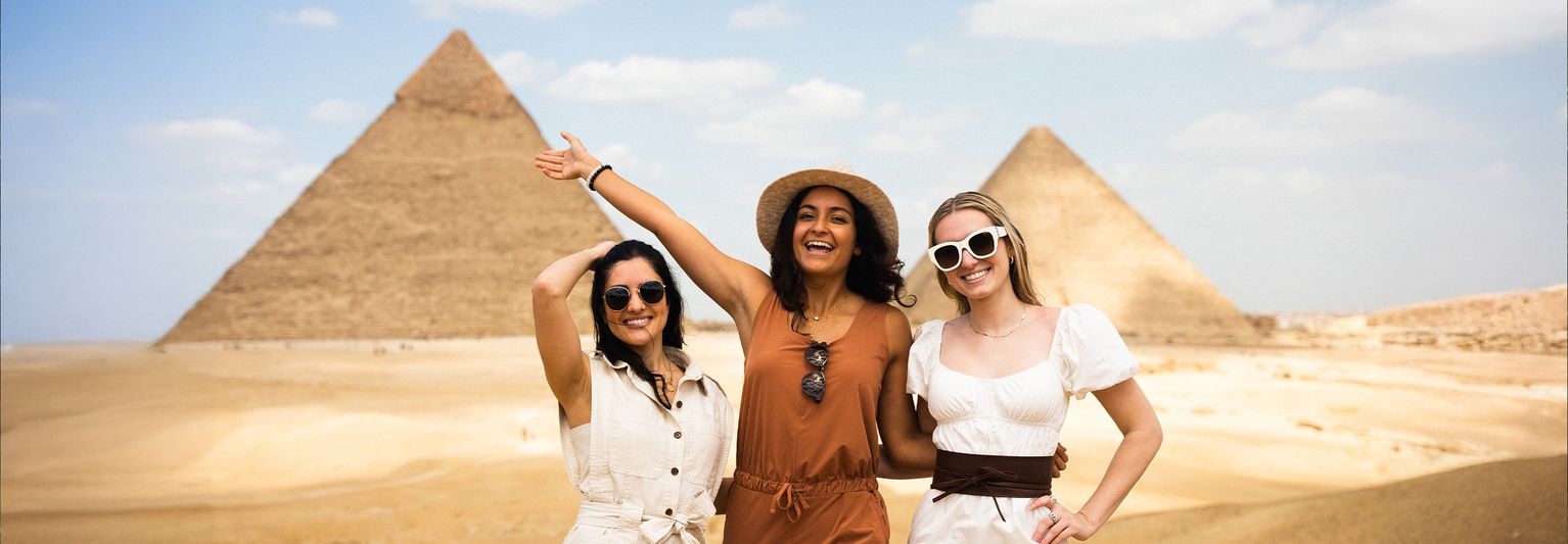 Three women posing in front of the pyramids of Egypt.