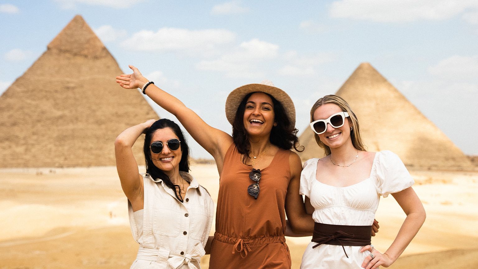Three women posing in front of the pyramids of Egypt.