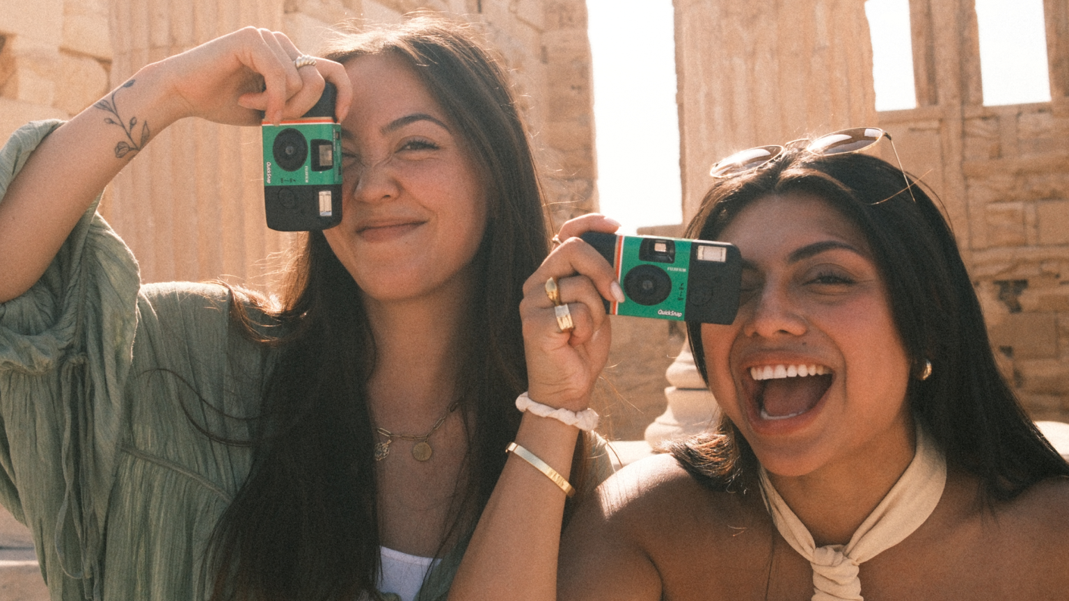 Two women holding up disposable cameras and standing in front of the Parthenon in Athens, Greece.