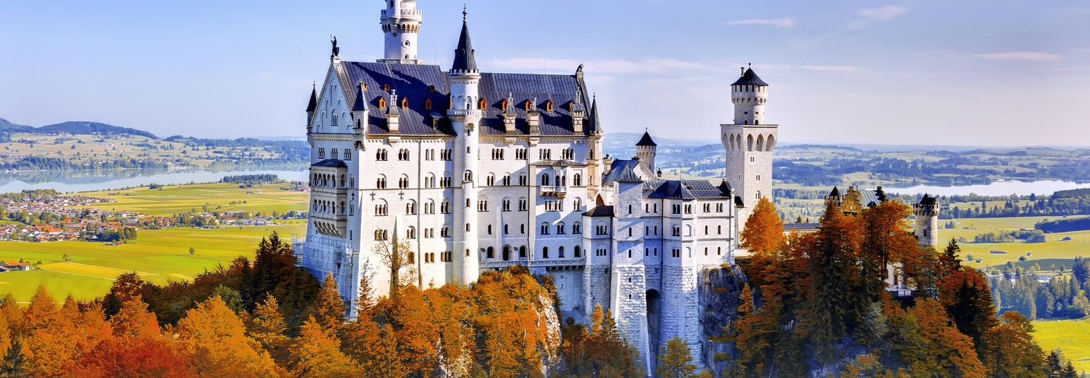 The hilltop castle of Neuschwanstein Castle in Germany with a river and open fields in the distanceon a sunny day