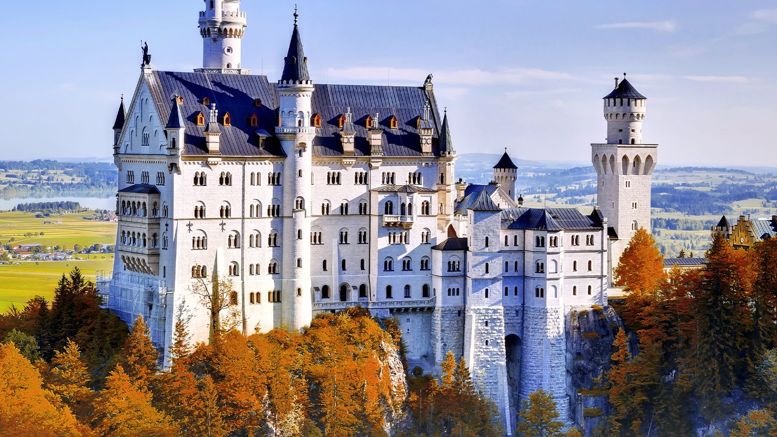 The hilltop castle of Neuschwanstein Castle in Germany with a river and open fields in the distanceon a sunny day