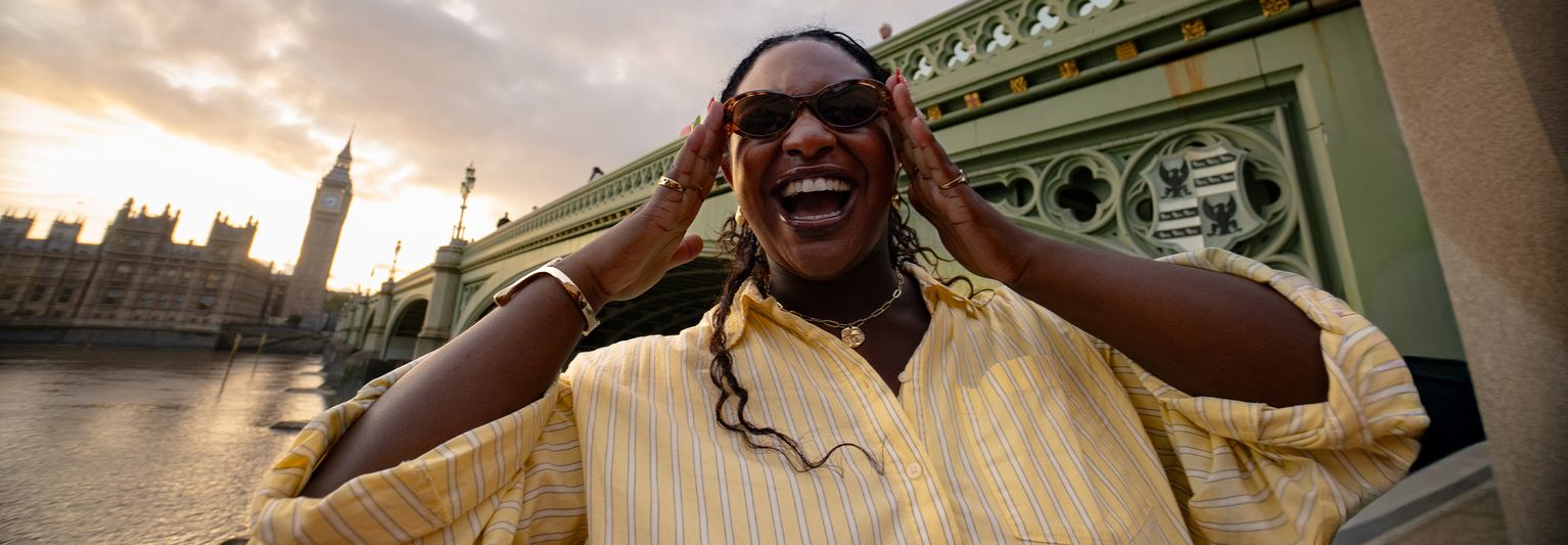 Woman posing with sunglasses in front of Westminster Bridge and Big Ben in London.