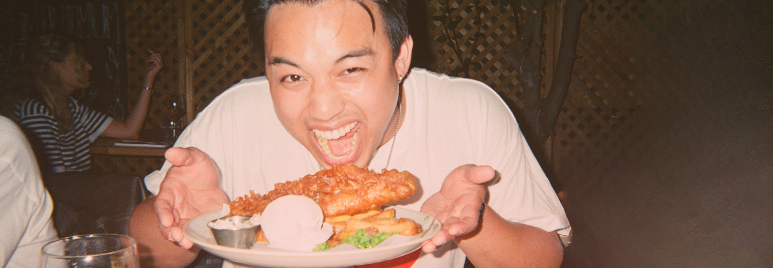 Person excitedly holding a plate of fish and chips, with a joyful expression, sitting at a table in a restaurant.