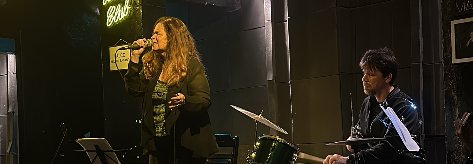 A woman singing Bossa Nova next to a man playing the drums.