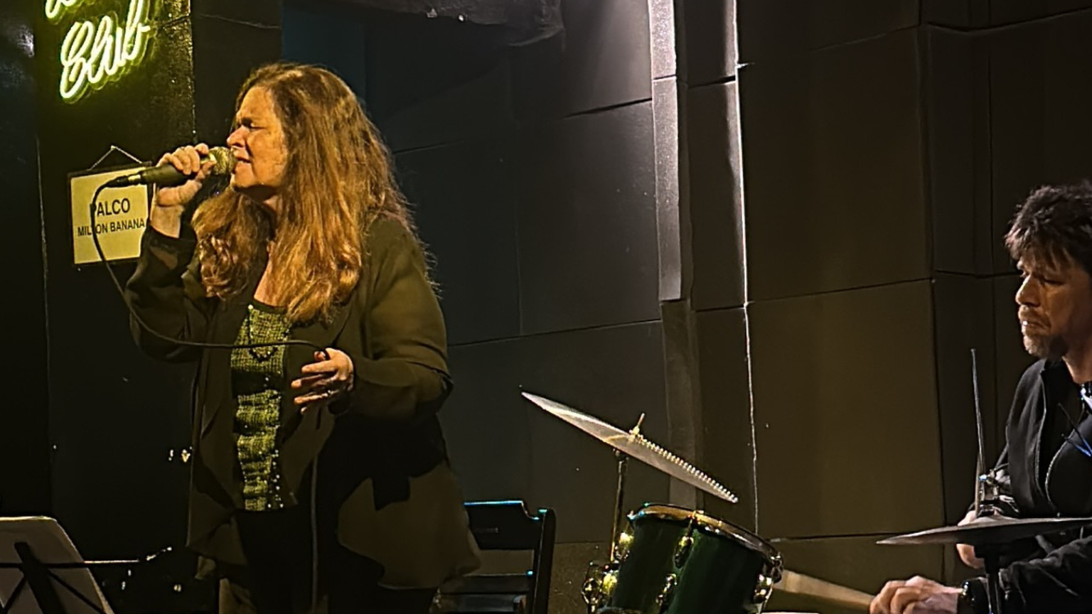 A woman singing Bossa Nova next to a man playing the drums.