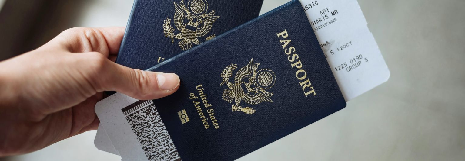 Hand holding two U.S. passports with boarding passes partially visible inside, against a neutral background.