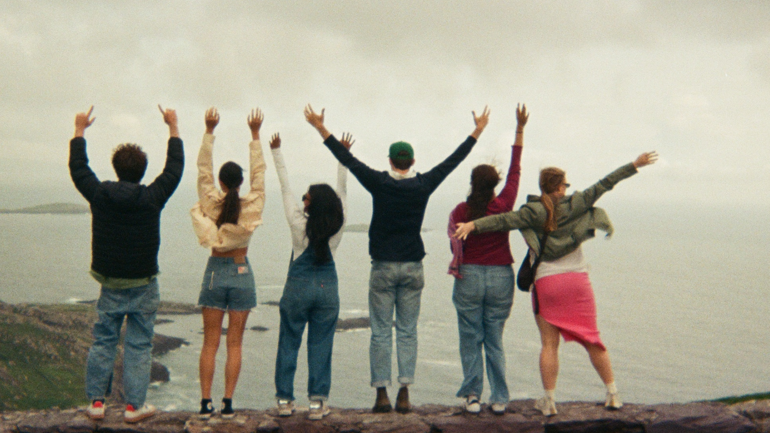 Six people on a cliff in Ireland facing away from the camera toward the ocean