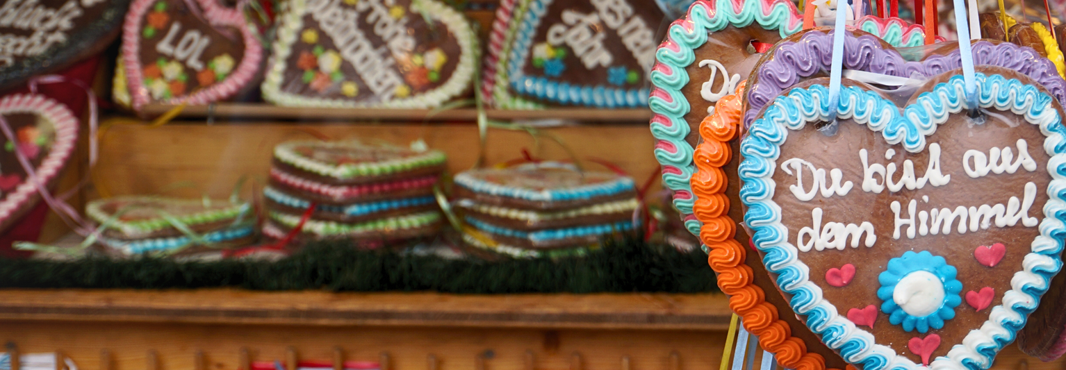 Heart-shaped gingerbread cookies with colorful icing and German text displayed at a market stall.