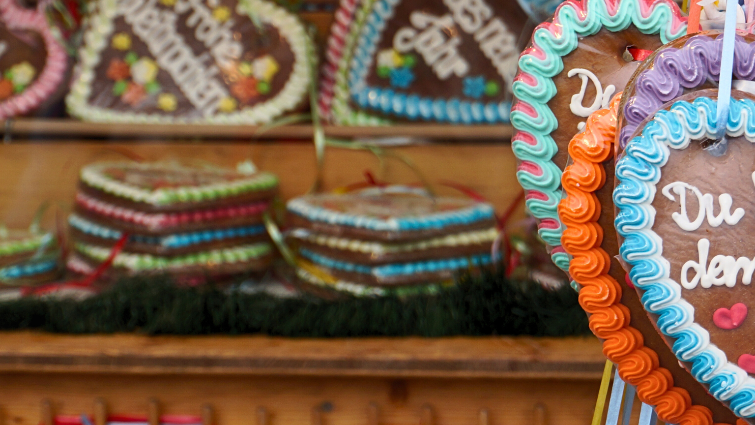 Heart-shaped gingerbread cookies with colorful icing and German text displayed at a market stall.