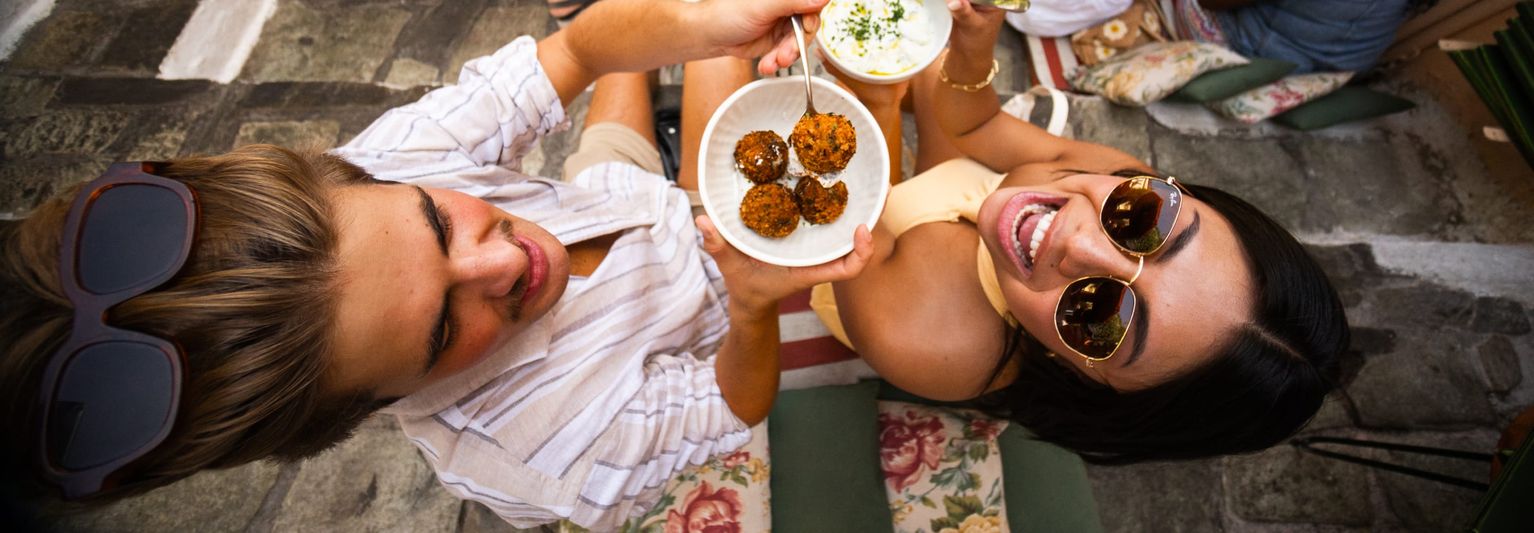 Two people looking up at the camera while sharing street food between them