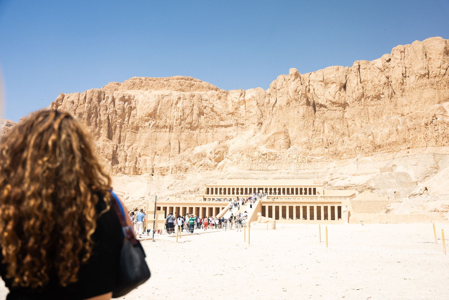 Woman standing in front of an Egyptian temple at the foot of a mountain on a sunny day