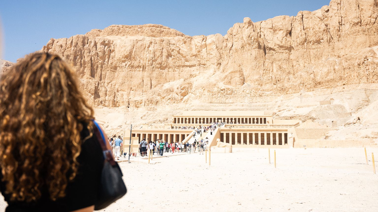 Woman standing in front of an Egyptian temple at the foot of a mountain on a sunny day