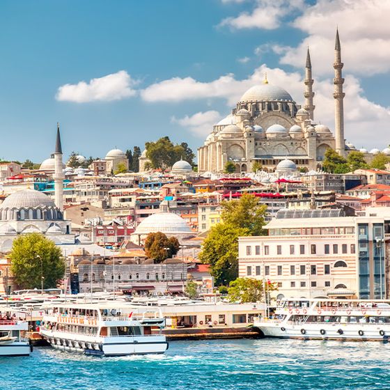 Scenic view of Istanbul with boats on the Bosphorus and the iconic Suleymaniye Mosque against a blue sky.