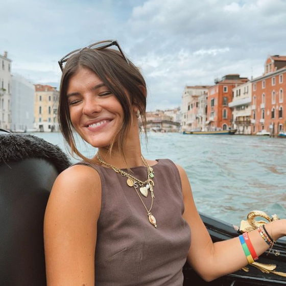 Woman smiling on a boat ride in Venice, with colorful buildings and cloudy sky in the background.