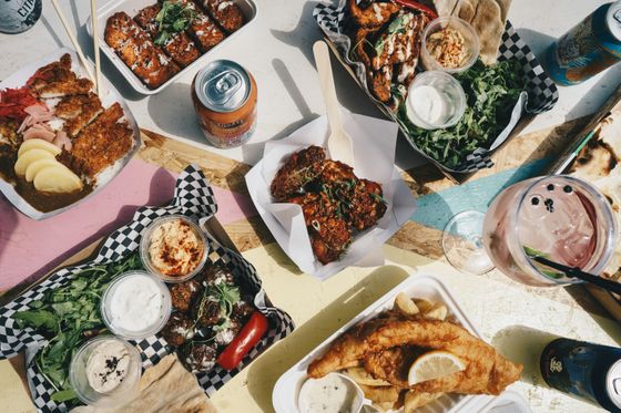 A colorful spread of various dishes including fried fish, wings, and sides, accompanied by drinks on a patterned table.