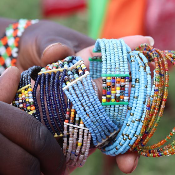 Close-up of hands holding colorful, intricately beaded bracelets with various patterns, including blue, orange, and multicolored designs.