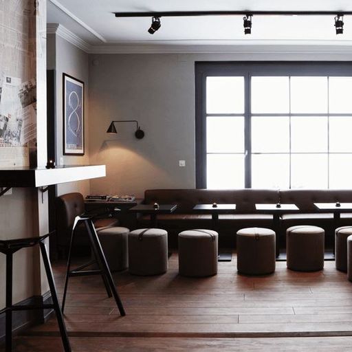 Minimalist cafe interior with modern furniture, a row of stools by a wall bench, wooden flooring, and a large window offering natural light.