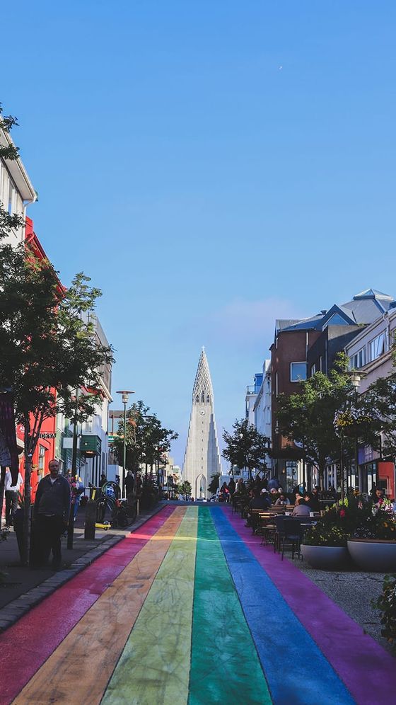 A vibrant rainbow path leads to the iconic Hallgrímskirkja church in Reykjavik, Iceland, with people enjoying the lively street atmosphere.