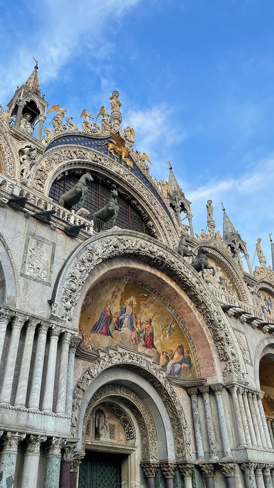 Ornate facade of St. Mark's Basilica in Venice, featuring intricate mosaics and detailed architectural sculptures under a clear blue sky.