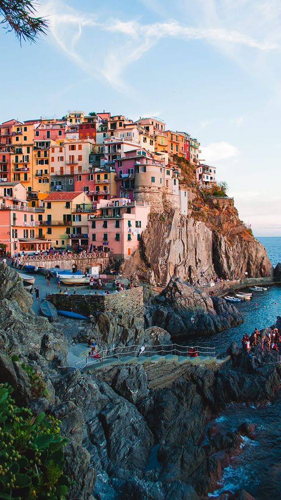 Cliffside village with colorful houses overlooking the sea, set on rugged rocks, with a serene blue sky and ocean in the background.