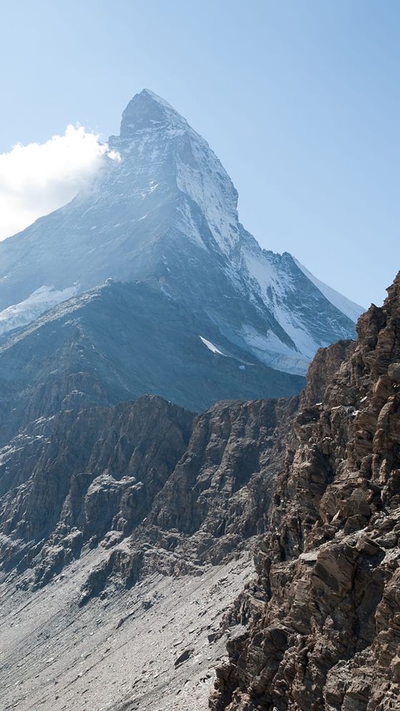 Snow-covered mountain peak under a clear blue sky, with rocky terrain in the foreground.