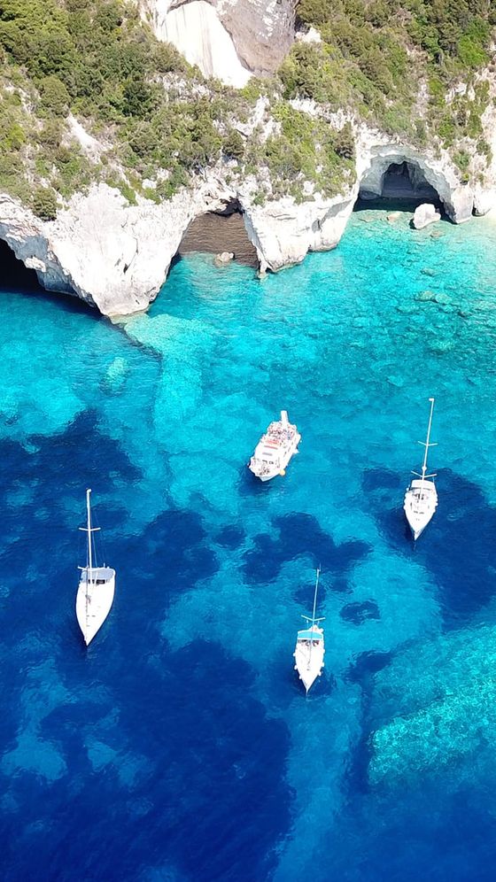 Four boats sail on vibrant turquoise and deep blue waters near rocky cliffs and caves, surrounded by lush greenery.