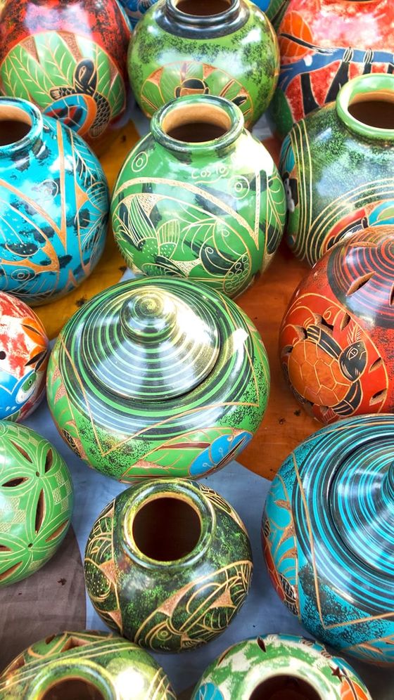 Colorful ceramic pots with intricate, vibrant patterns and designs, featuring greens, blues, reds, and earth tones, displayed on a surface.