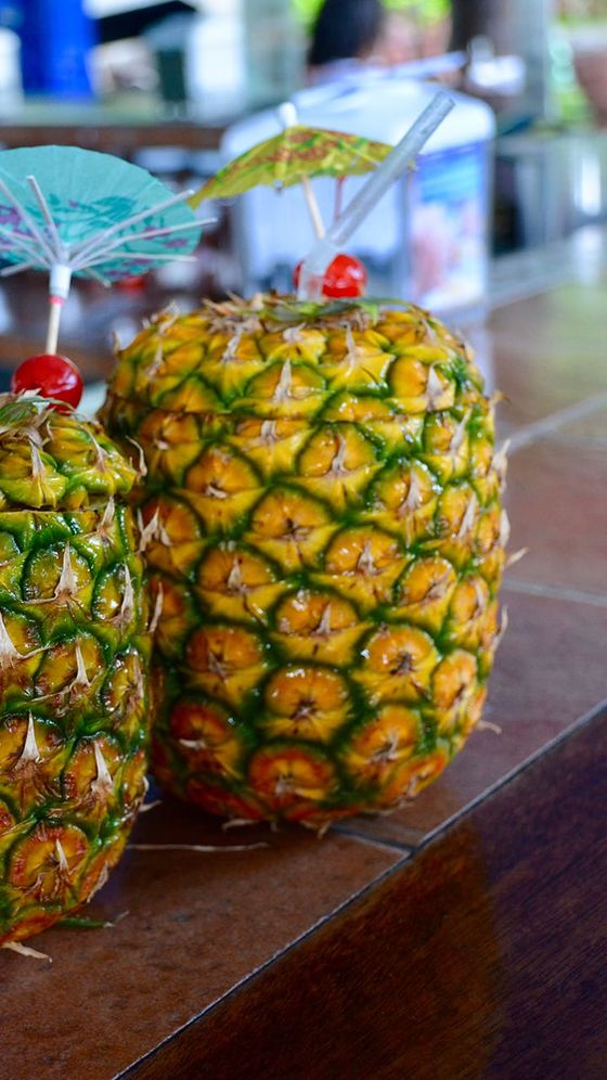Two hollowed pineapples with cocktail umbrellas and cherries on top, placed on a wooden counter.