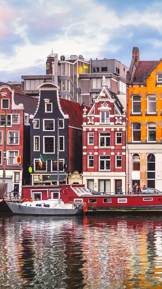 Colorful, historic canal houses with ornate facades are reflected in the water in Amsterdam.