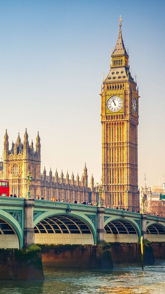 Big Ben clock tower and parts of the Palace of Westminster next to the River Thames with Westminster Bridge and a red double-decker bus.