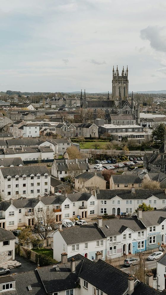 Aerial view of a town with rows of houses and a large cathedral in the background under a cloudy sky.