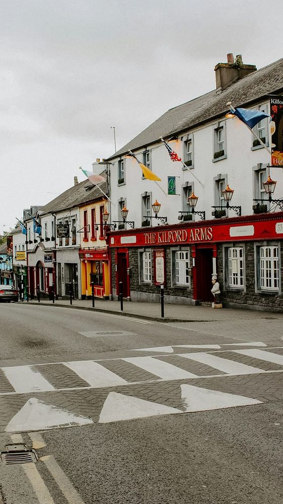 A street view of a small town with colorful buildings, including The Kilford Arms, and road markings in the foreground.