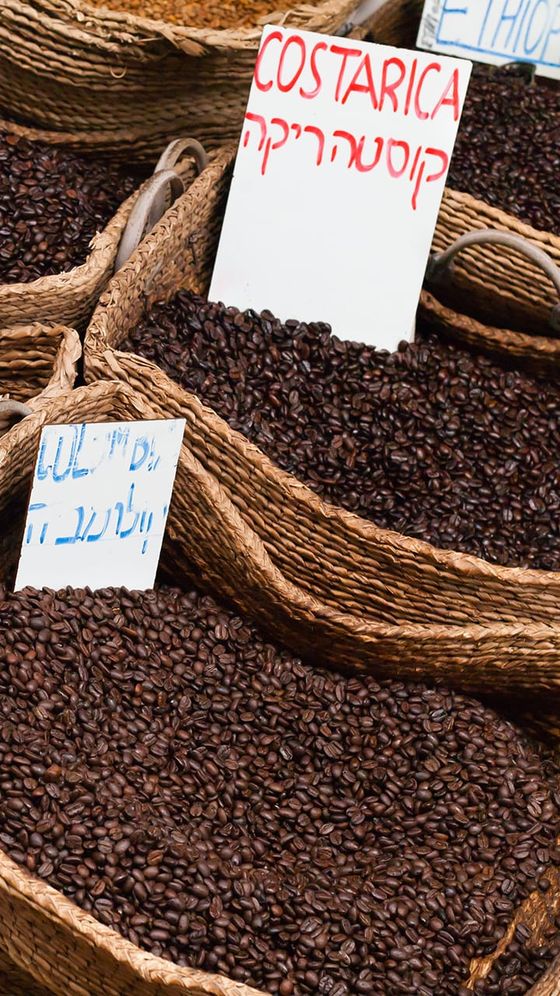 Baskets of coffee beans labeled with various origins, including Costa Rica and Ethiopia, displayed at a market.