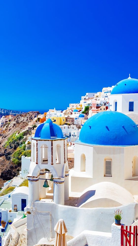 Scenic view of Santorini, Greece, featuring white buildings with blue domes against a clear blue sky and colorful hillside architecture.