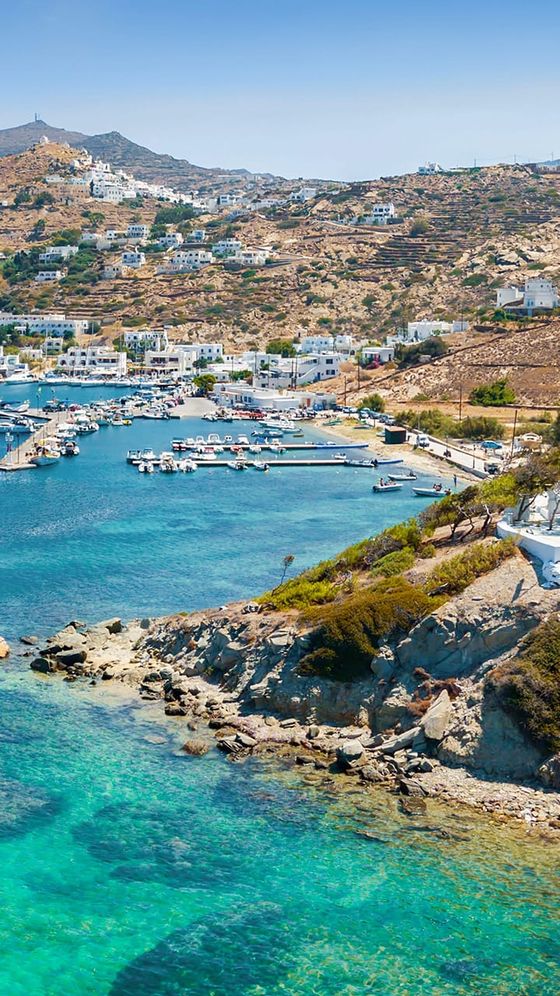 Idyllic coastal scene with a turquoise bay, rocky shoreline, and hillside dotted with white buildings under a clear blue sky.