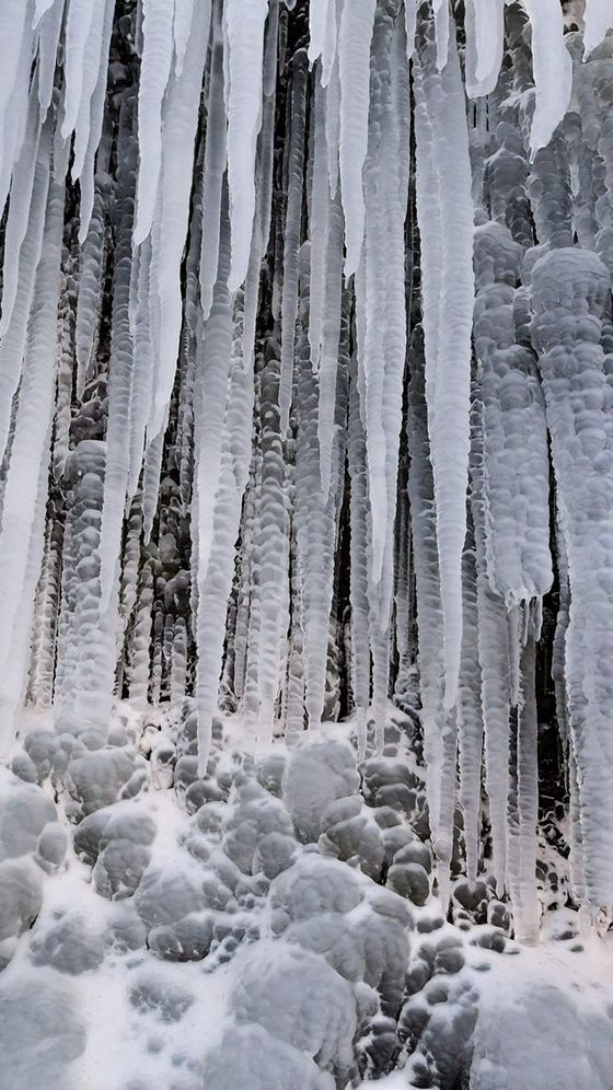 Long icicles hanging in front of a rocky surface covered in ice, creating a wintry, textured scene.