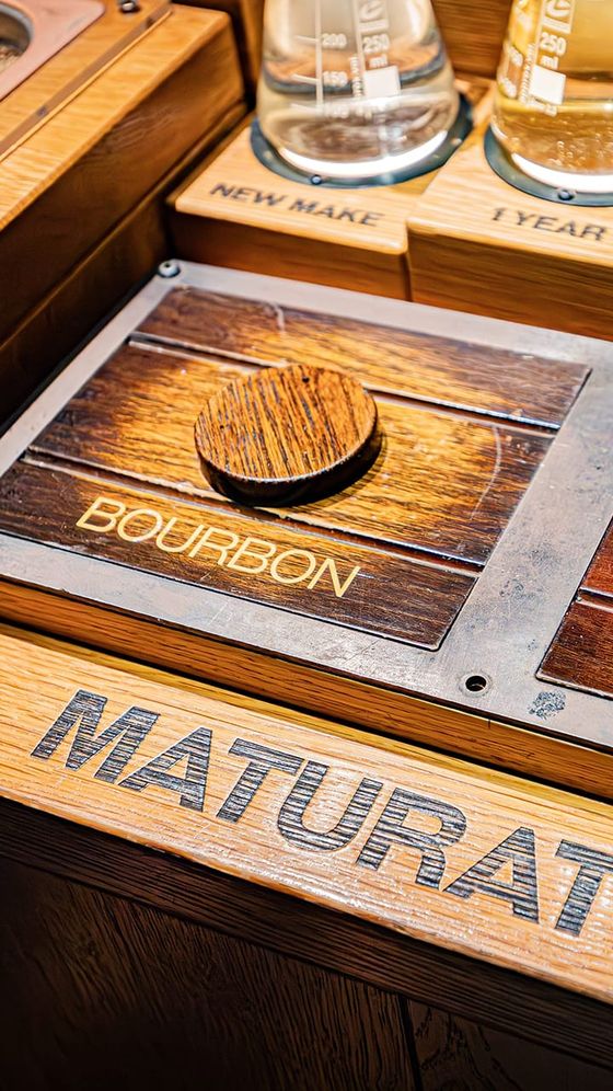 Close-up of a wooden display showcasing a bourbon barrel lid with labeled sections "New Make," "1 Year," and "Maturation" on wooden panels.