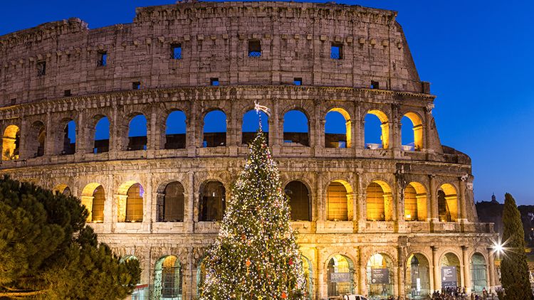 The Colosseum at dusk with a large, decorated Christmas tree in the foreground, illuminated by warm lights.