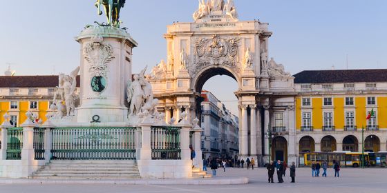 The Praça do Comércio in Lisbon with the Arco da Rua Augusta, a statue, and people walking in the square under a clear sky.